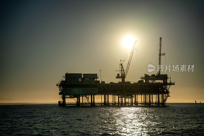 在一个晴朗的早晨，在加州长滩/洛杉矶附近，黄昏时分关闭海上石油和天然气钻井平台与远处的货船